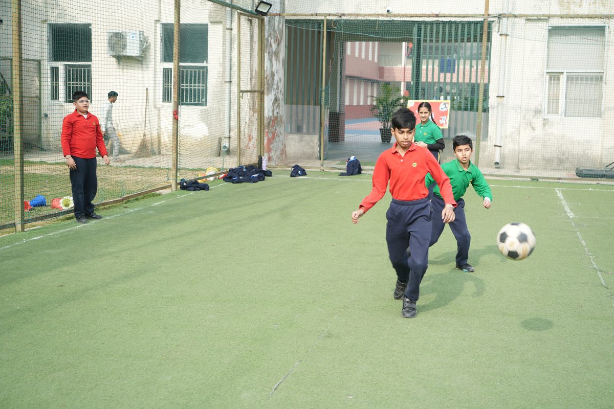 Young students in house colours chase a football during an inter-house match on the turf at TSUS Sarabha Nagar