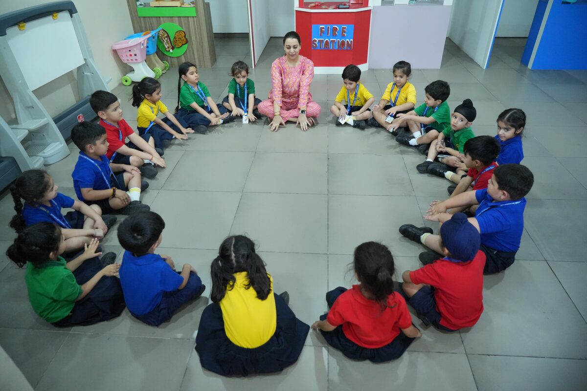 A teacher sitting on the floor with a circle of young children during a classroom activity at TSUS Sarabha Nagar