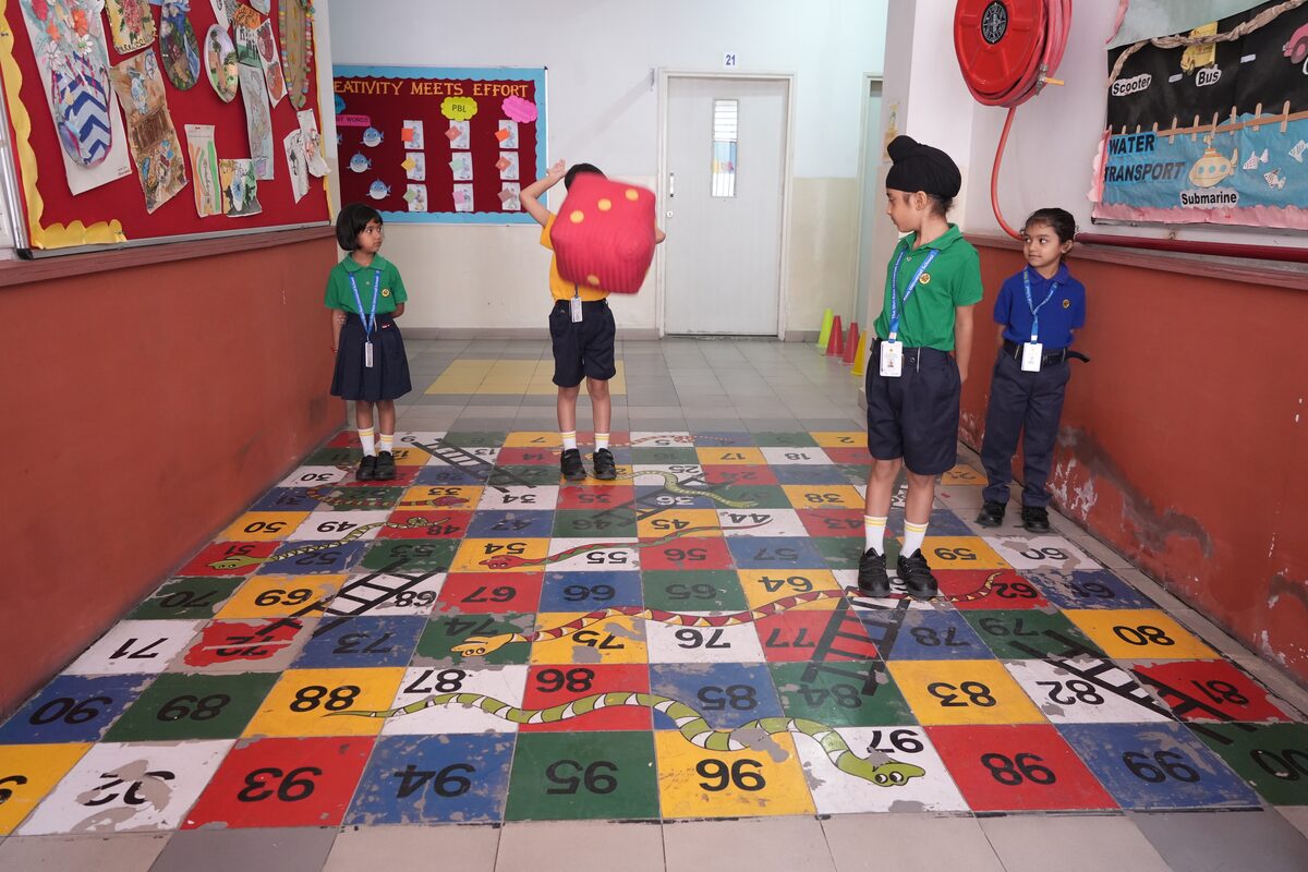 Four children playing a giant snakes and ladders game painted on a school corridor floor, one holding a big soft dice